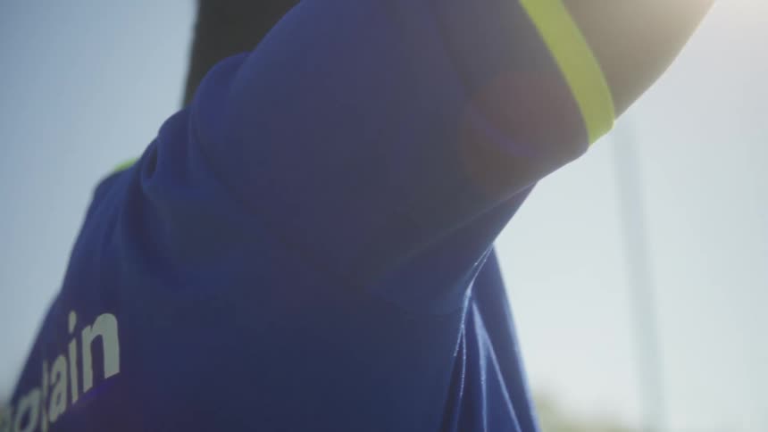 Man in blue shirt with yellow collar looks at field under clear sky with greenery in background