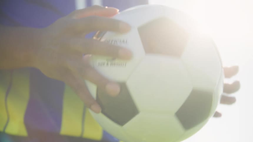 Young black man wearing a jersey holding a soccer ball on his hand outdoors during day time