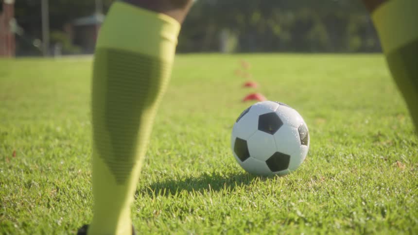 Male legs standing on a field in front of a soccer ball outdoors during day time