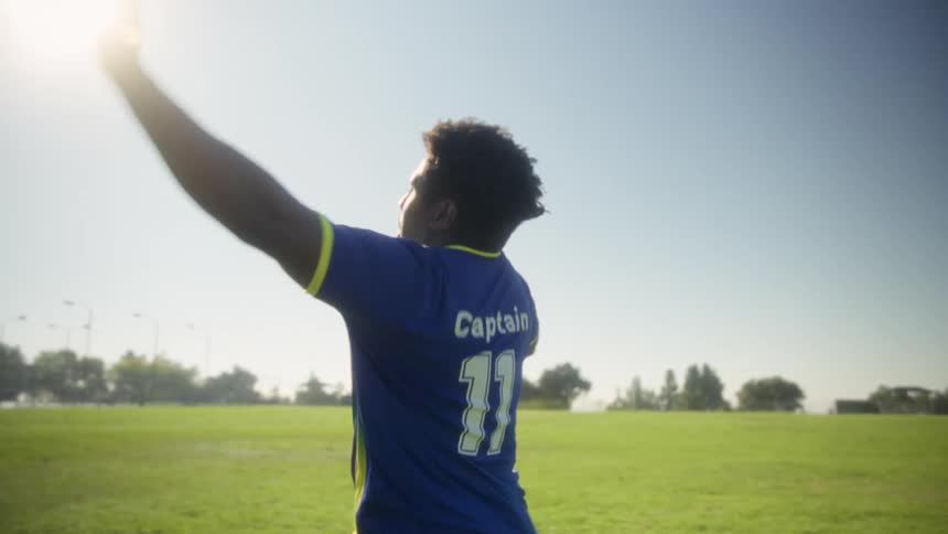 The video shows a soccer player wearing a blue and yellow jersey with the number 11 on a sunny fieldinitially he looks intense then turns away before transitioning into celebrating excitedly with jumps and cheers culminating in him clapping and po
