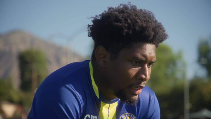Young black man wearing a soccer uniform squatting on a field and panting with a tired facial expression outdoors during day time