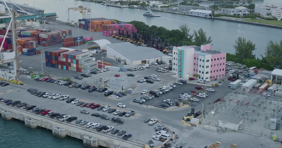A seaport filled with stacked containers and numerous cars parked in the lot surrounded by ocean water