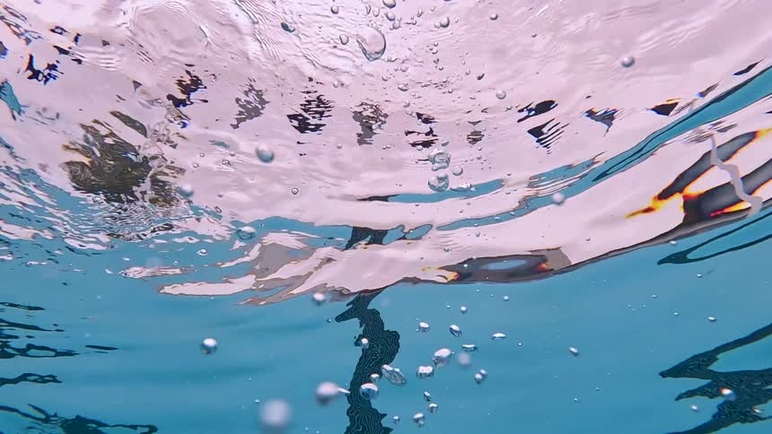 An underwater view of a pool surface capturing numerous bubbles and lane markers with light reflecting on the pinkishclear water