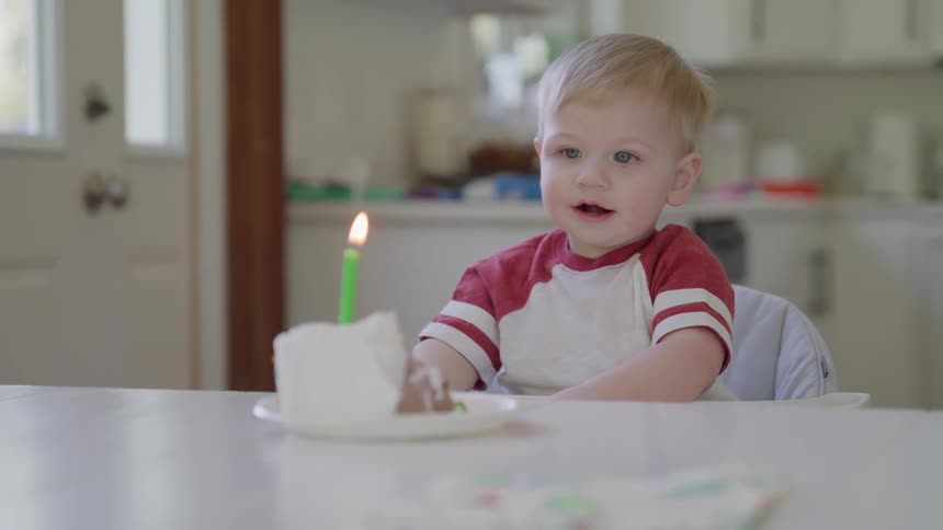 Child seated in front of a slice of cake with a lit candle