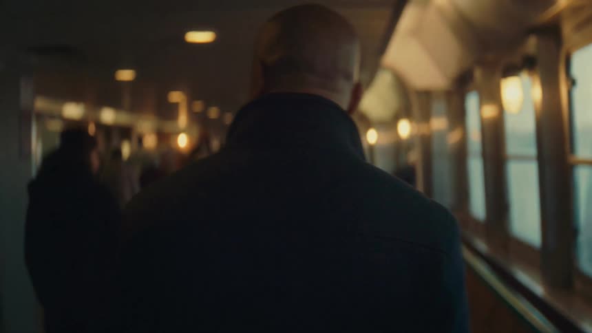 Person walking through an indoor corridor with lit windows beside them