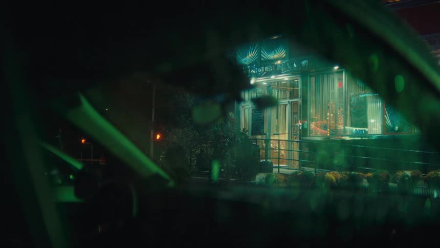 A view through a car window shows a brightly lit diner exterior at night