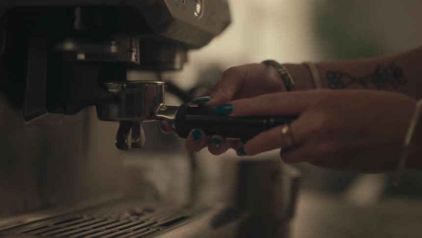 The hands of a person with operating a metal portafilter on an espresso machine