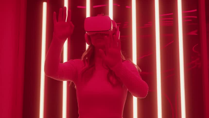 Young adult woman gesturing around while wearing a vr headset in a room with colorful lights indoors
