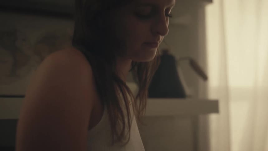 A closeup of a teenage girl with hands resting in her lap showing her jewelry and bright nail polish the girl with a concerned expression while sitting indoors dressed in a white top and a floral skirt