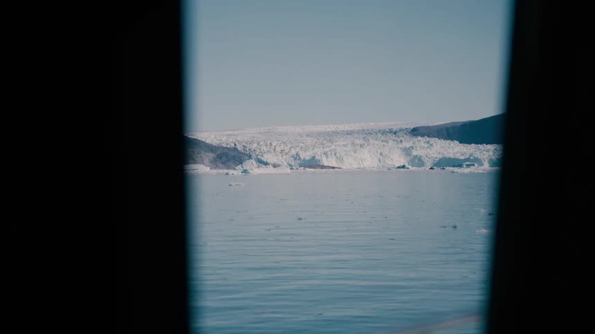 View through the window of a ship of melting ice on arctic water and a glacier in the distance