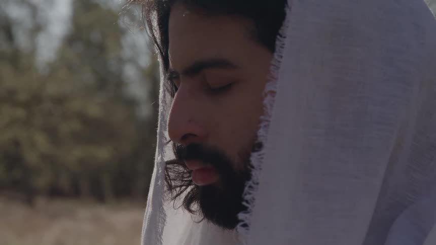 Bearded man with a light mantle covering his head in an outdoor area