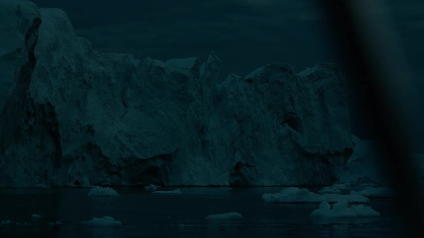 A large jagged iceberg formation looms over dark ocean water and smaller ice chunks under a dimly lit dark blue sky