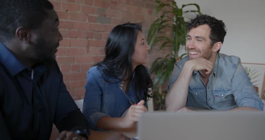 Two men and a woman talk around a laptop