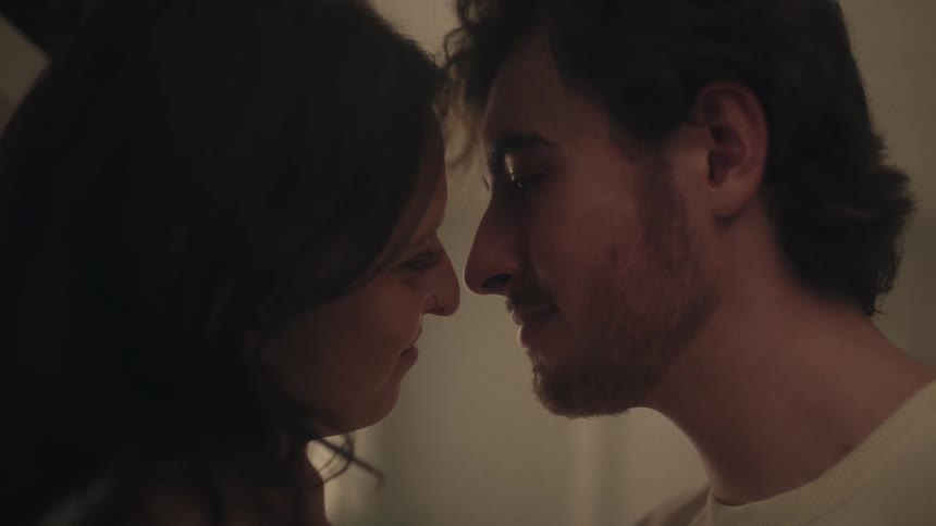 A young couple shares a tender intimate kiss in soft low light indoors