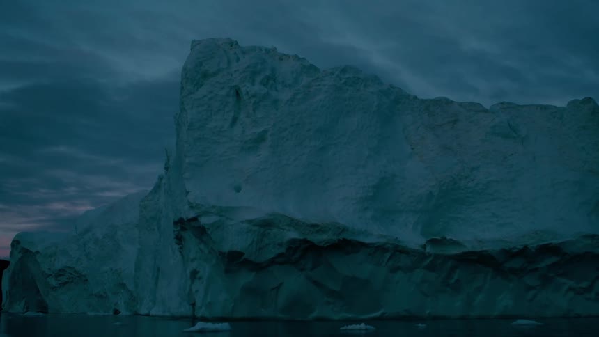 A boat approaching an artic coast covered in ice outdoors during dusk or dawn
