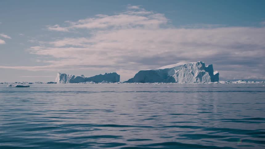 Sun shining on glaciers as melting ice floats across arctic water