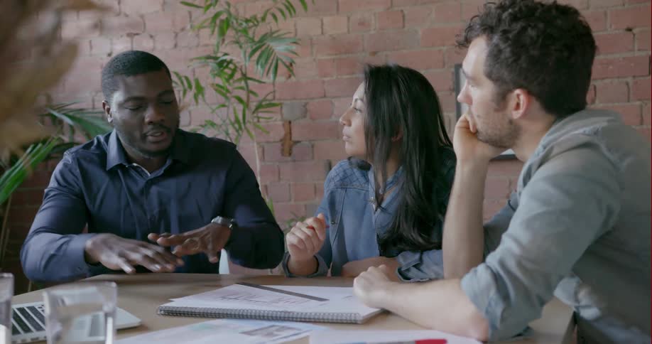Three people chat around a table at work