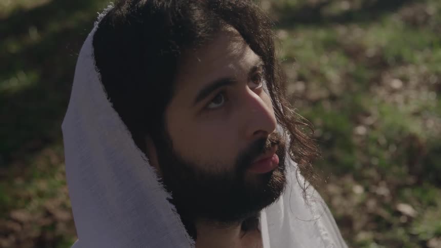 Bearded young man with a white veil over his head looking up with a contemplative facial expression outdoors during day time