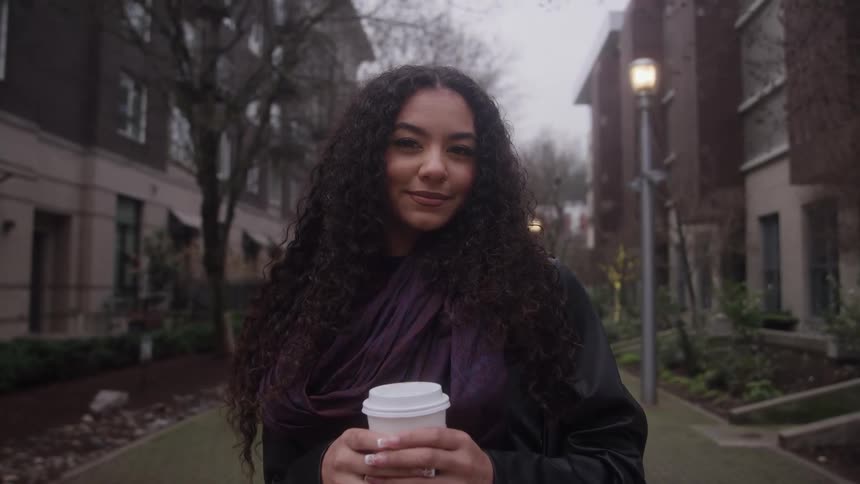 A woman is standing outside in front of apartment buildings holding a cup of coffee