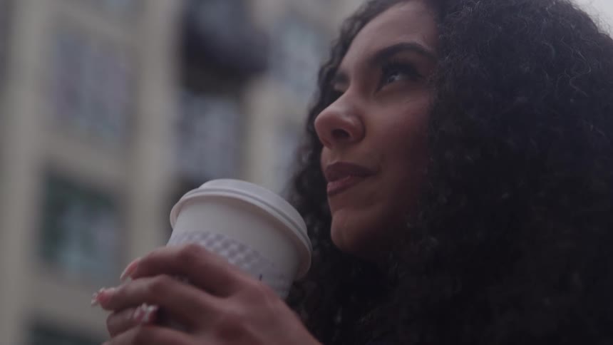 Young female biracial person drinking coffee from a disposable cup in an urban area outdoors during day time