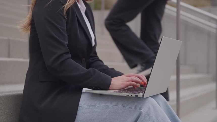 Woman sitting on the steps outside of a building typing on her laptop computer
