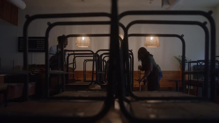 Two workers meticulously clean the dimly lit cafe interior after closing hours