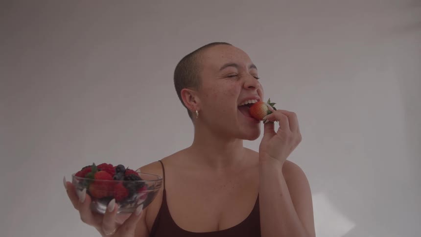 The woman is eating strawberries and smiling