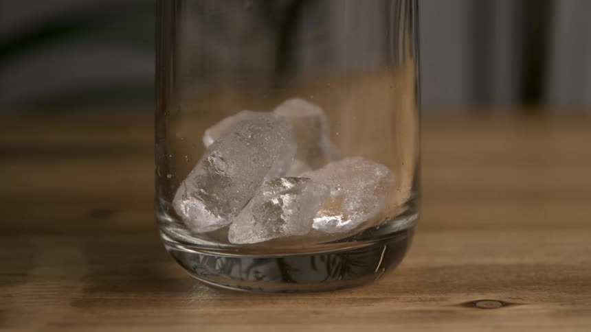 Several ice cubes tumble into an empty glass clinking together as they settle at the bottom