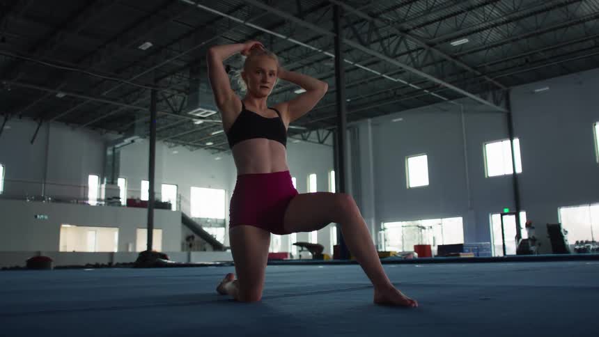 Young adult woman arranging her hair while stretching on a mat at the gym indoors during day time