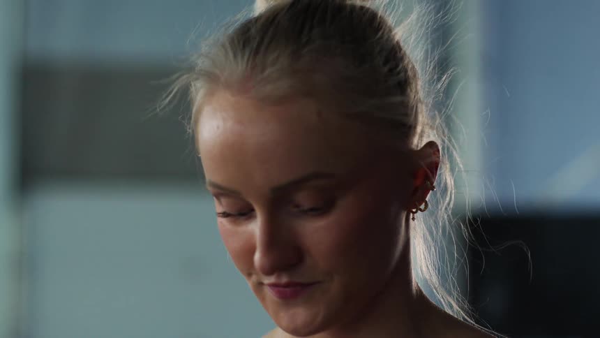 A blonde woman with her hair in a bun in shown from the neck up looking down and around nervously