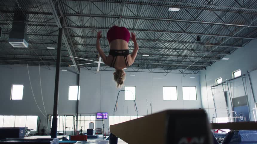 A teenage gymnast is doing a backflip on the balance beam in a gym