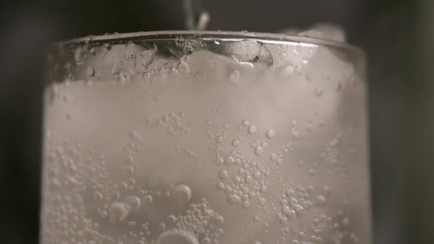 Bubbles rise through ice cold soda in a condensation covered glass