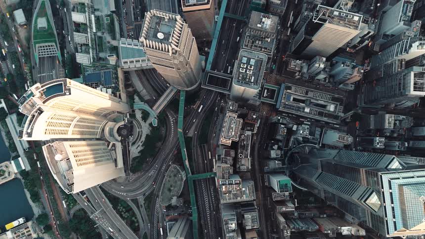 An extreme aerial view looks down upon a dense modern cityscape of tall buildings and winding highways during the day