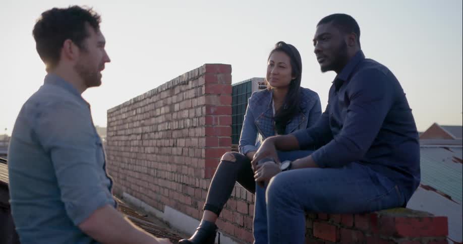 Two men and a woman outside by a brick wall talking