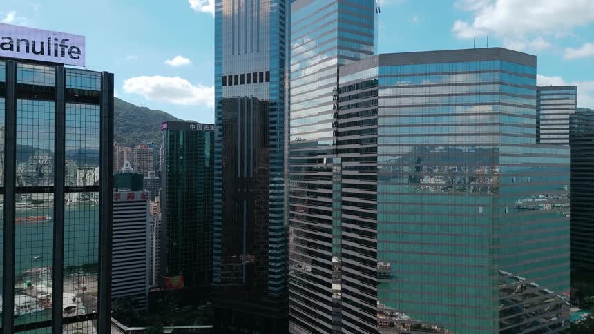Skyscrapers on a metropolitan area with a green hill on the background and the reflection of a bay with a body of water on the glass of the buildings outdoors during day time