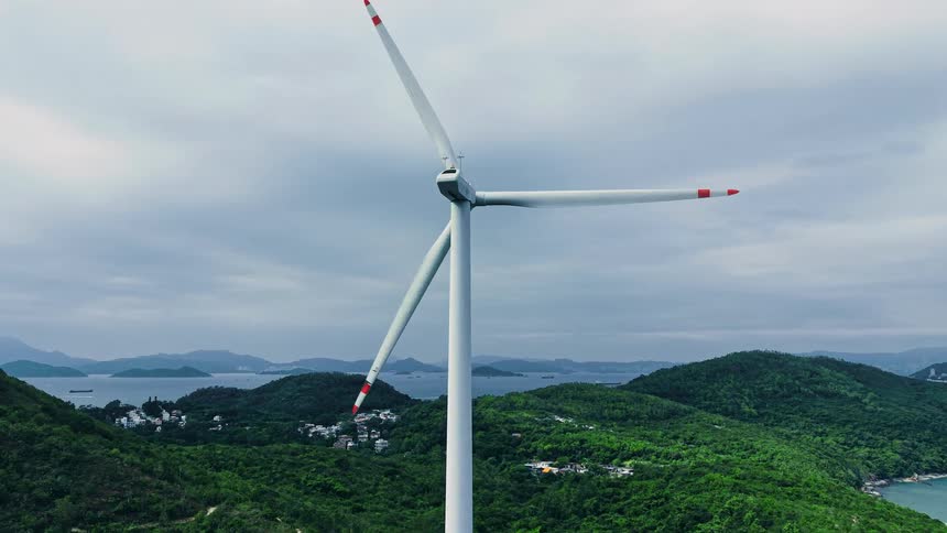 Wind turbine positioned among green hills overlooking the sea
