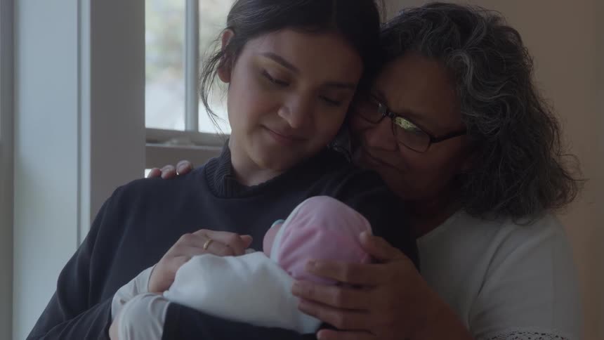 Two women share a tender moment cradling a newborn baby together