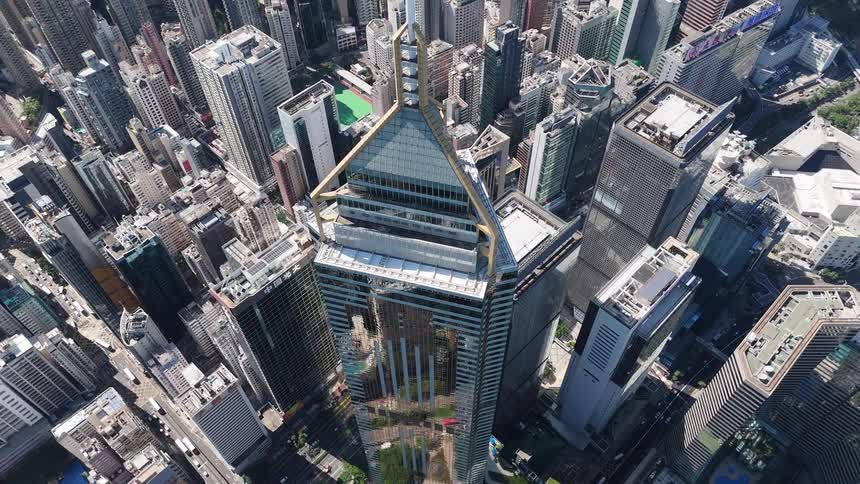 Aerial view of a tall glass skyscraper rising over a dense city skyline