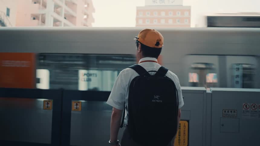 Businessman with a backpack waiting at a metro station with a moving train on the platform