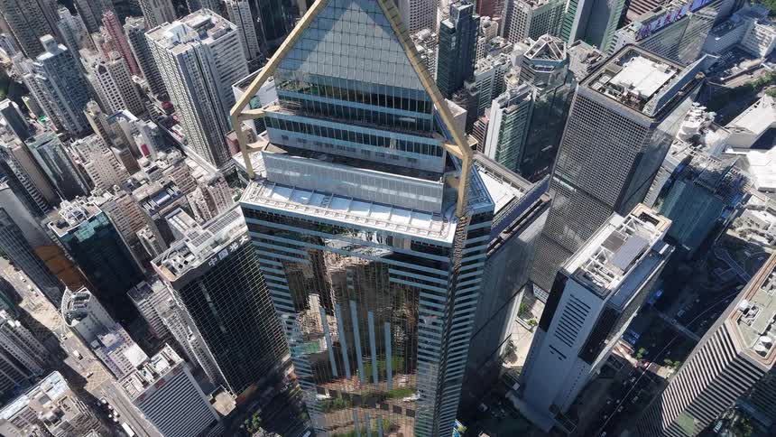 Descending from a dizzying height the view glides down the reflective glass faade of a towering skyscraper showcasing its golden spire amidst a dense concrete jungle