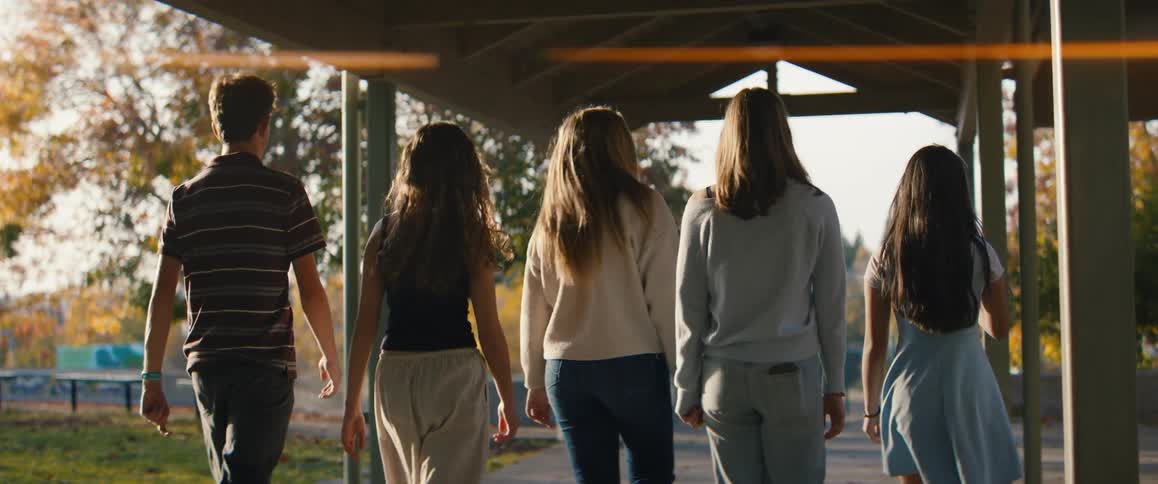 Four female teenager and a male teenager walking together on a walkway at a part during dusk or dawn