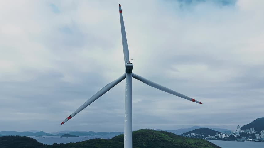 The windmill is slowly turning on the hills across the water from the city