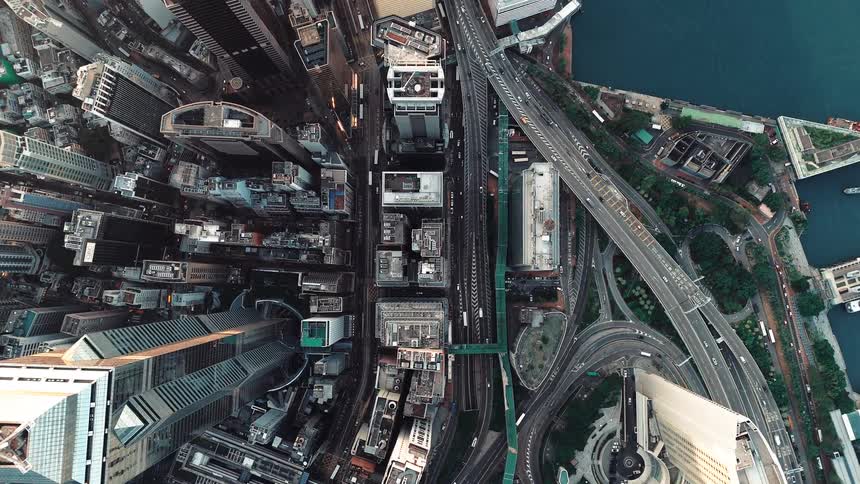 A highangle aerial drone shot looks straight down onto a dense metropolitan city center featuring skyscrapers and winding highway traffic near a harbor