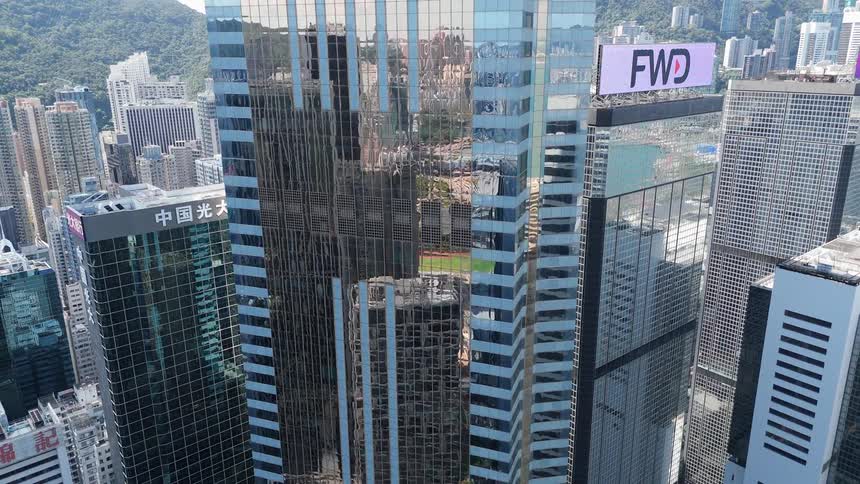 Glass skyscraper reflecting surrounding buildings in a dense urban area