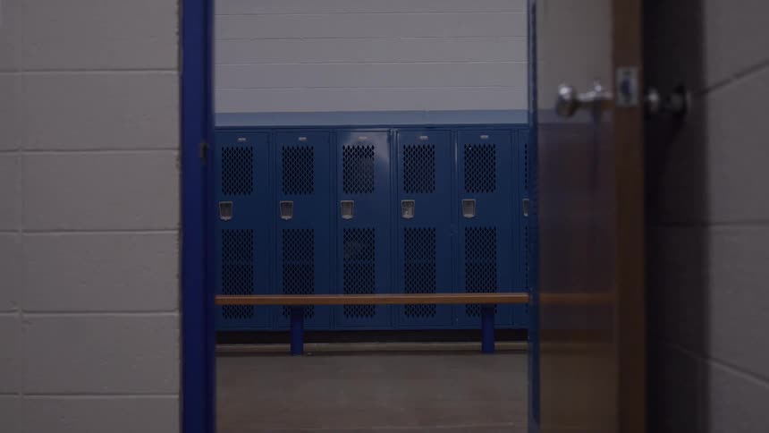 Empty locker room with blue lockers seen through the doorway