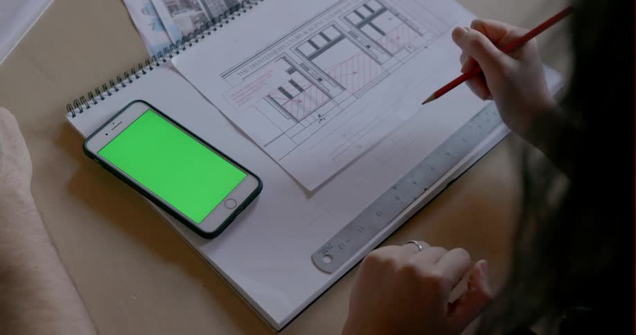 A woman uses a smartphone and ruler to make a sketch in a notebook