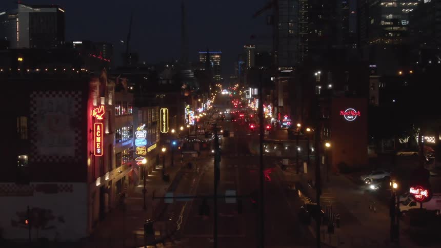 This is a wide elevated nighttime shot looking down a city street lined with buildings that feature brightly lit neon signs characteristic of an entertainment districtthe street slopes gently uphill toward a dark background dominated by modern high