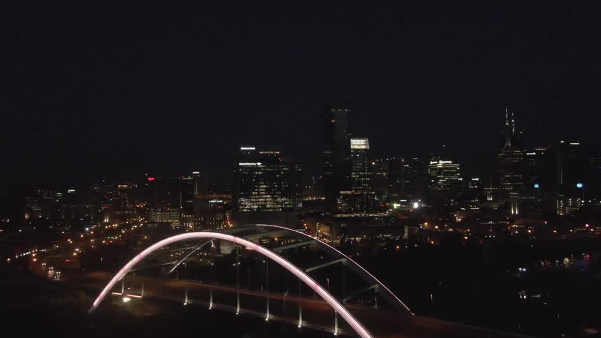 A glowing arched bridge spans the foreground as the camera glides toward a glittering city skyline alive with the movement of night traffic and skyscraper lights