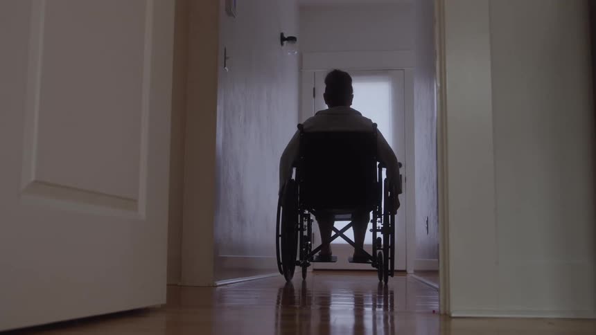 Woman sitting in a wheelchair wheels herself down a corridor in her home during the daytime