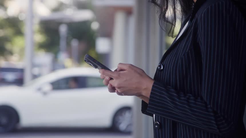 Woman using a smartphone while standing outdoors with a white car in the background